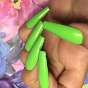 May include: Close-up of a hand wearing five long, bright green, glossy, artificial fingernails.