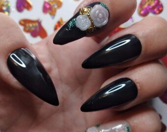 May include: Black stiletto nails with white and green 3D flower embellishments.