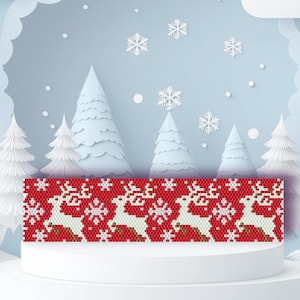 May include: A red and white beaded Christmas pattern featuring reindeer and snowflakes. The design is displayed on a white pedestal against a backdrop of stylized winter trees and falling snowflakes, evoking a festive holiday theme.