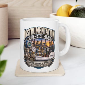 Könnte beinhalten: Ein weißer Keramikbecher mit einer Grafik einer Industrieanlage, dem Text "INSTRUMENTATION TECHNICIAN" oben und "MEASURE CONTROL OPTIMIZE" sowie "PEOPLE PROCESS SAFETY" unten, umgeben von verschiedenen technischen Geräten.