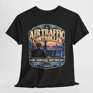 Op de afbeelding: Een zwart t-shirt met een afbeelding van een luchtverkeersleider aan een werkstation. Het ontwerp bevat de tekst AIR TRAFFIC CONTROLLER en GUIDE COORDINATE KEEP THEM SAFE, met een uitzicht op een landingsbaan bij zonsondergang.