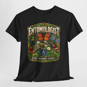 Könnte beinhalten: Ein schwarzes T-Shirt mit einer farbenfrohen Grafik verschiedener Insekten, darunter ein Schmetterling, ein Käfer und eine Libelle, die eine Lupe über einer Biene umgeben. Der Text lautet ENTOMOLOGIST oben und STUDY DISCOVER CLASSIFY unten.