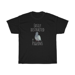 May include: Black t-shirt with white text that reads "Easily Distracted by Pigeons". A cartoon pigeon is pictured below the text.