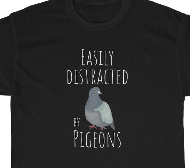 May include: Black t-shirt with white text that reads "Easily Distracted by Pigeons". A cartoon pigeon is pictured below the text.