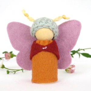 May include: A handcrafted felt butterfly doll with a wooden head. The doll features a light blue knitted cap, orange body, red shawl, and large pink wings. Yellow yarn antennae extend from the cap. A whimsical, handcrafted item.