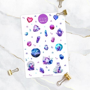 Peut inclure: Une feuille d'autocollants illustrant des cristaux et des pierres précieuses en aquarelle dans des tons de violet, bleu et rose. Les autocollants sont sur un fond blanc avec quelques petites formes géométriques noires et blanches. Le texte "Art Tales Studio" et "Crystals 039" est imprimé sur la feuille.
