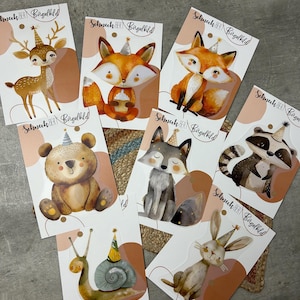 Könnte beinhalten: Ein Set mit acht Bügelbildern, die verschiedene Waldtiere mit Partyhüten zeigen. Die Tiere sind ein Reh, ein Fuchs, ein Bär, ein Waschbär, ein Wolf, eine Schnecke und ein Kaninchen. Jedes Bügelbild hat den Text "Schneck BERT Bügelbild" aufgedruckt.