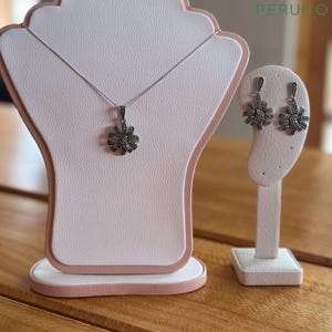 May include: A silver necklace and earrings set with a marigold-shaped pendant and matching earrings. The pendant and earrings are adorned with black marcasite stones.