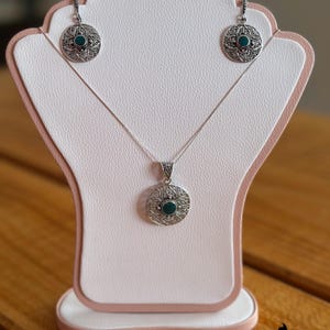 May include: A silver necklace and earrings set with a green stone pendant and matching earrings. The pendant and earrings feature a filigree design.