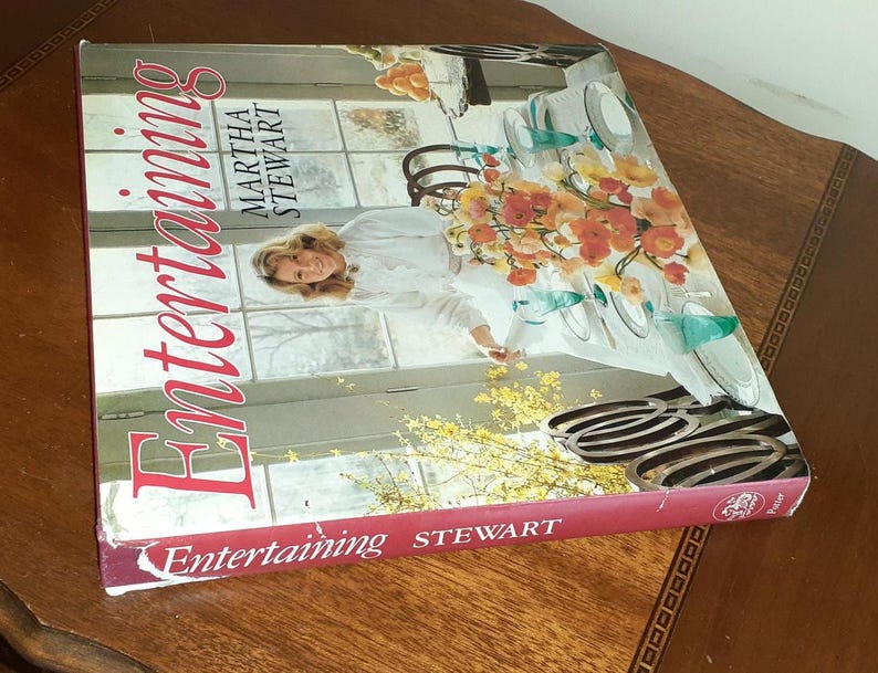 May include: A red hardcover book titled "Entertaining" by Martha Stewart. The cover features a woman in a white shirt and a floral arrangement on a table with plates and glasses.