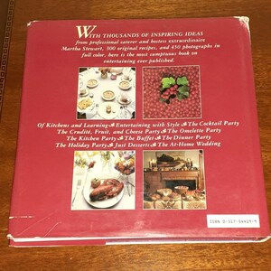 May include: A red book cover with the title "With Thousands of Inspiring Ideas" and the author "Martha Stewart". The book cover features images of food and table settings, including a lobster, fruit, and a fireplace.