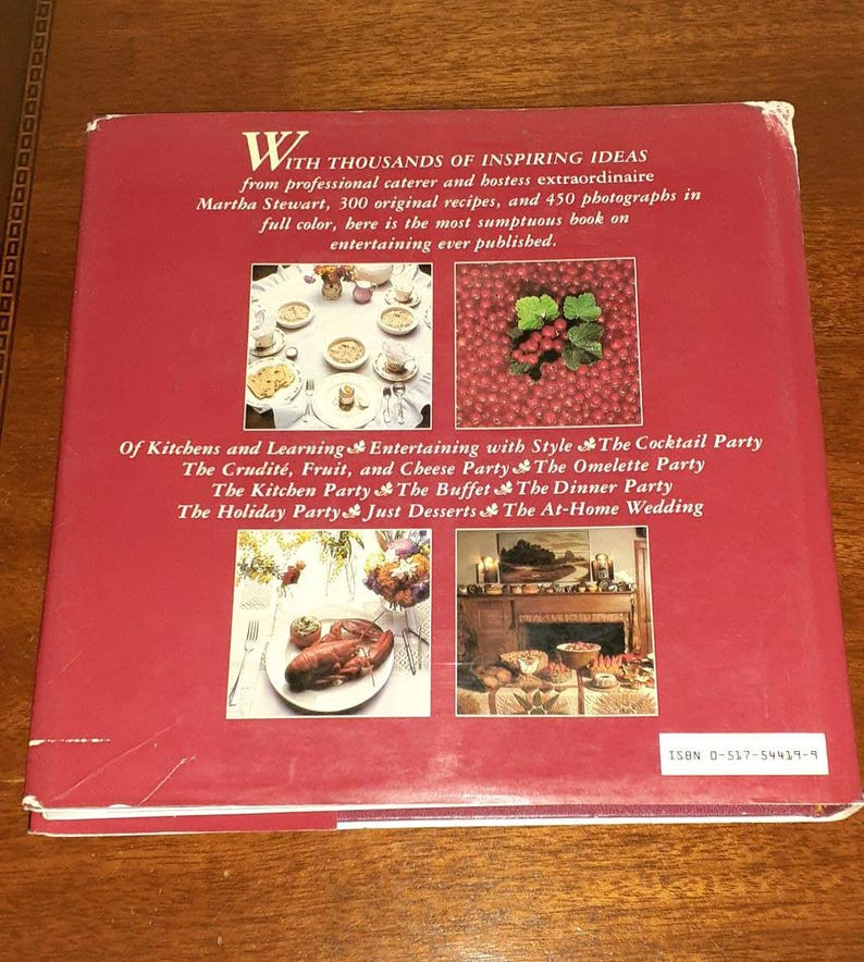 May include: A red book cover with the title "With Thousands of Inspiring Ideas" and the author "Martha Stewart". The book cover features images of food and table settings, including a lobster, fruit, and a fireplace.