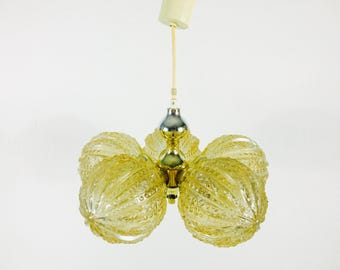 May include: A vintage, mid-century modern chandelier with a gold and silver finish. The light fixture has five textured, globe-shaped shades in a pale yellow color. The chandelier is suspended from a white ceiling fixture.