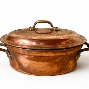 Op de afbeelding: Een witte keramische mok met een zwarte handgreep en de tekst "But First, Coffee" in een vetgedrukte, zwarte letter. De mok staat tegen een vage achtergrond, wat een gezellige setting suggereert.