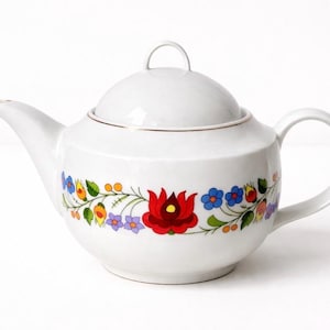 Peut inclure: Une théière en céramique blanche avec un corps arrondi, un couvercle assorti muni d'une petite poignée et un bec verseur incurvé. L'extérieur est orné d'une bande horizontale de motifs floraux colorés, incluant des fleurs rouges, bleues et jaunes.