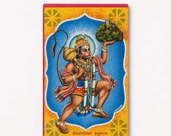 May include: A rectangular print featuring a central illustration of a deity with a tail, holding a golden mace and a mountain. The figure wears a crown, jewellery, and patterned clothing against a blue background. The text Sankatmochan Hanuman is visible.