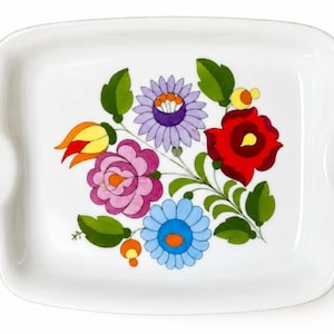 May include: A rectangular white ceramic serving tray with integrated side handles. The centre features a colourful floral illustration with a large red flower, a purple flower, a pink flower, a light blue flower, and green leaves.