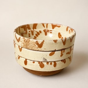 May include: A stack of three ceramic bowls. The bowls have a cream-colored base with a brown, organic pattern around the rim. The bottom of the bowls are a darker brown color. The bowls are stacked on top of each other.