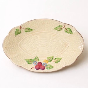 Peut inclure: Assiette ovale en céramique blanc cassé avec une surface texturée. L'assiette présente un motif décoratif de feuilles vertes, de baies rouges et de petites fleurs bleues et jaunes. Le bord est marron.