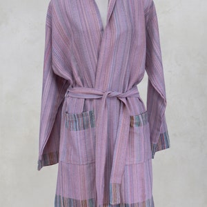 Peut inclure: Peignoir à capuche lilas avec des rayures verticales de différentes couleurs. La robe a une ceinture assortie, deux poches avant et des franges colorées à l'ourlet. Le peignoir est présenté sur un mannequin.