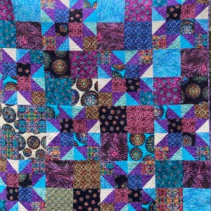 May include: A patchwork quilt with a star pattern. The quilt features squares of various patterned fabrics in shades of blue, purple, teal, and cream. The quilt is machine quilted with a repeating pattern.