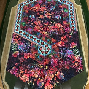 May include: A hexagonal table runner with a black background and a colorful floral pattern. The runner has a blue and white border with a geometric design.