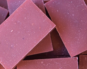 May include: A close-up of several bars of handmade soap. The soap is a light pink color and has a speckled appearance.