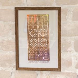 May include: A framed print of a geometric design in shades of gold and brown. The design is made up of repeating squares and triangles. The print is titled "PLAYROOM CMXNO ORL12 - 12" with the text "FRANK LLOYD WRIGHT" below.