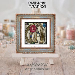 May include: A framed cross-stitch pattern of a Glasgow Rose design, displayed on a small easel. The artwork features a red rose, blue and purple accents, and the text "Glasgow Rose" and "Pevote Stitch Pattern". The frame has a distressed blue and gold finish.