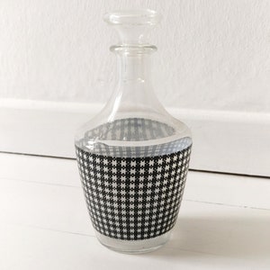 Könnte beinhalten: Eine klare Glaskaraffe mit einem schwarz-weißen Karomuster um die Mitte.