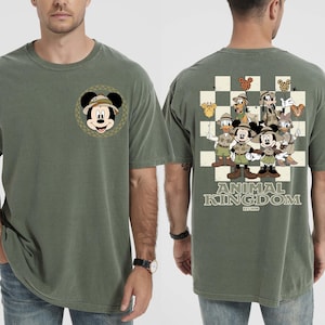 May include: Olive green t-shirt with a Mickey Mouse graphic wearing a safari hat on the front. The back features a checkered design with Disney characters in safari outfits, and the text "ANIMAL KINGDOM" and "EST. 1998".