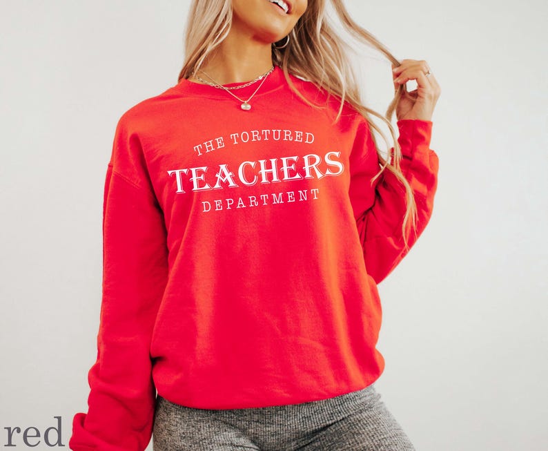 Puede incluir: Una sudadera roja con el texto "THE TORTURED TEACHERS DEPARTMENT" en letras blancas. La sudadera es de color rojo liso y tiene mangas largas. La modelo lleva pantalones grises.