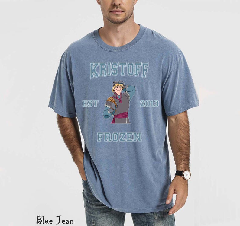 May include: A blue t-shirt featuring the word "KRISTOFF" above an illustration of the character from the movie Frozen. The shirt also includes the text "EST 2013 FROZEN". The shirt is a solid blue color.