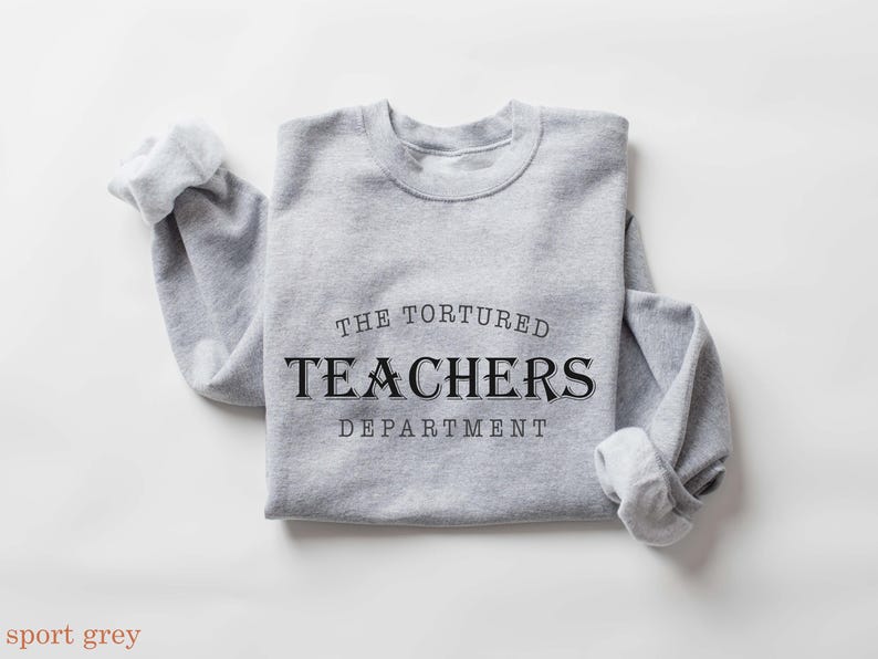 Puede incluir: Una sudadera gris claro con el texto "THE TORTURED TEACHERS DEPARTMENT" en negro. Las mangas est&aacute;n dobladas. Las palabras "sport grey" est&aacute;n en la parte inferior de la imagen. La sudadera est&aacute; doblada.