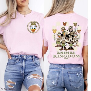 May include: A pale pink t-shirt with a Daisy Duck design on the front and a Disney character group graphic with "ANIMAL KINGDOM" on the back. The tee has a round neck and short sleeves.