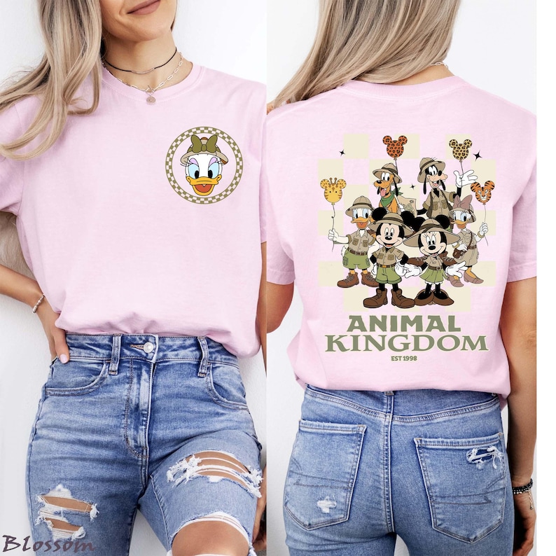 May include: A pale pink t-shirt with a Daisy Duck design on the front and a Disney character group graphic with "ANIMAL KINGDOM" on the back. The tee has a round neck and short sleeves.