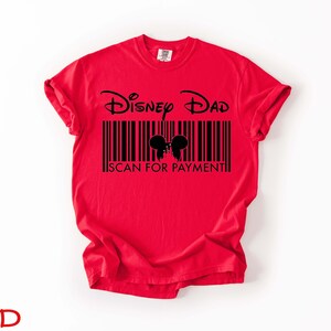 K&ouml;nnte beinhalten: Ein rotes T-Shirt mit den Worten "Disney Dad" &uuml;ber einem Barcode-Design mit Mickey Mouse Ohren. Der Text "SCAN FOR PAYMENT" befindet sich darunter. Das Wort "RED" steht unten.