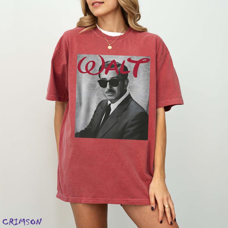 May include: A crimson red short-sleeve t-shirt featuring a black and white graphic print of a man in a suit and sunglasses. The text "WALT" is printed in a red script font above the portrait. The shirt has a crew neckline and a relaxed fit.