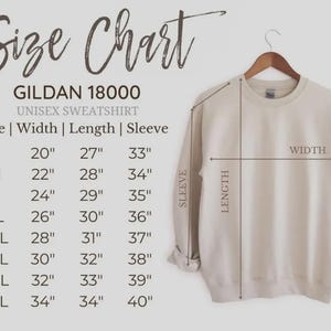 Puede incluir: Una sudadera unisex Gildan 18000 de color crema cuelga de una percha de madera. La imagen incluye una tabla de tallas con medidas en pulgadas para el ancho, el largo y el largo de la manga, que van desde la talla S hasta la 5XL.