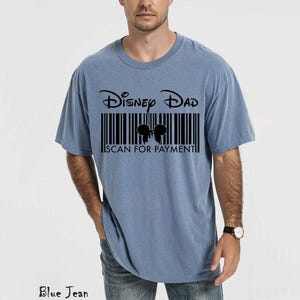 K&ouml;nnte beinhalten: Hellblaues T-Shirt mit dem Text "Disney Dad" &uuml;ber einem Barcode-Design. Der Barcode enth&auml;lt eine Silhouette von Mickey Mouse-Ohren und die Worte "SCAN FOR PAYMENT".