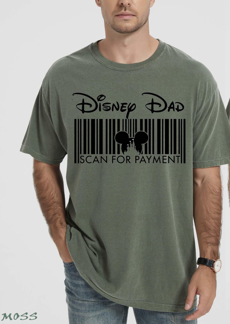 K&ouml;nnte beinhalten: Olivgr&uuml;nes T-Shirt mit dem Text "Disney Dad" &uuml;ber einem Barcode-Design. Der Barcode enth&auml;lt eine Silhouette von Mickey Mouse-Ohren und den Text "SCAN FOR PAYMENT".