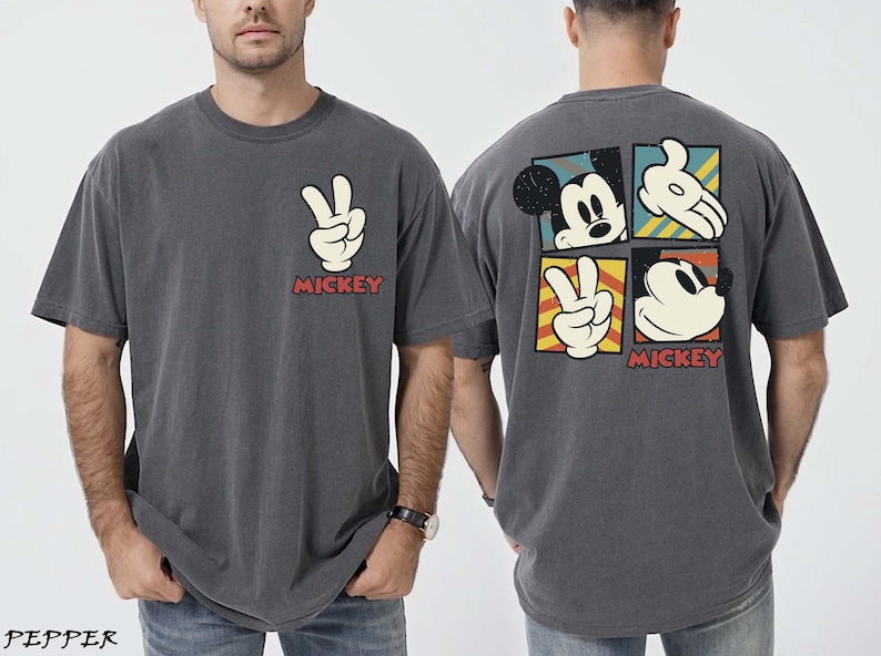 May include: Dark grey t-shirt with a white peace sign and the word "MICKEY" in red. The back features Mickey Mouse graphics in a square grid. A casual, vintage-style tee, suitable for everyday wear.