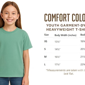 K&ouml;nnte beinhalten: Ein junger Mensch tr&auml;gt ein gr&uuml;nes Comfort Colors Youth Garment-Dyed Heavyweight T-Shirt. Das Shirt hat einen Rundhalsausschnitt und kurze &Auml;rmel. Das Bild enth&auml;lt eine Gr&ouml;&szlig;entabelle mit Ma&szlig;en in cm.