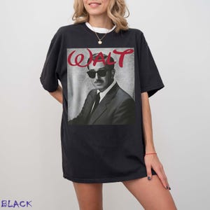 May include: A black short-sleeved t-shirt featuring a graphic print of a man in a suit and sunglasses. Above the figure, the word WALT is printed in a red, stylized script font. The background of the graphic has a subtle, light gray damask pattern.