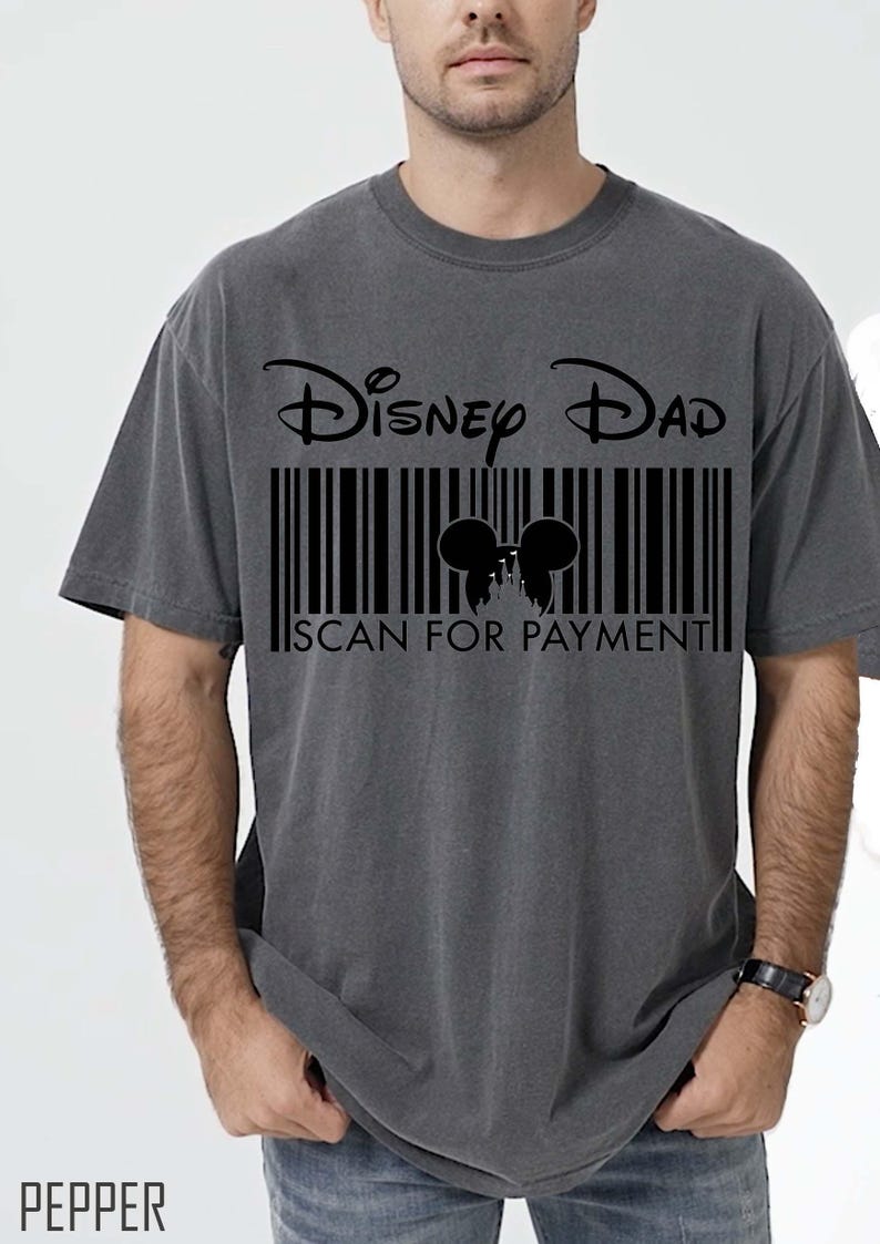 K&ouml;nnte beinhalten: Dunkelgraues T-Shirt mit der Aufschrift "Disney Dad" &uuml;ber einem schwarzen Barcode-Design. Der Barcode enth&auml;lt eine Silhouette von Mickey Mouse-Ohren und den Text "SCAN FOR PAYMENT".
