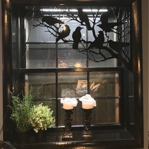 May include: A black window frame with a white window pane and a black metal silhouette of crows on a branch. Two white candles are on the window sill.