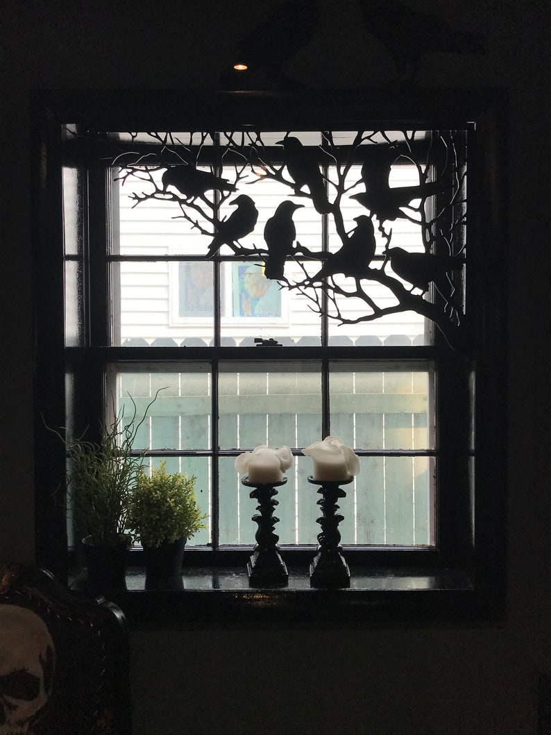 May include: A black window with a metal silhouette of a tree branch with crows perched on it. Two black candle holders with white candles are on the window sill.