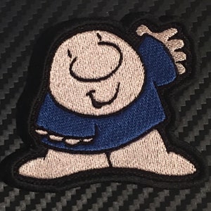 May include: Embroidered patch of a cartoon character with a white body, blue shirt, and a smiling face. The character is standing with one hand raised.