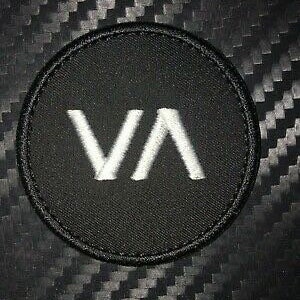 May include: Black round patch with white embroidered letters "VA" in the center.