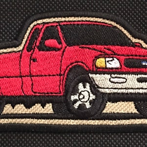 May include: Red embroidered patch of a pickup truck with a black interior and a white front bumper. The truck has a tan background.